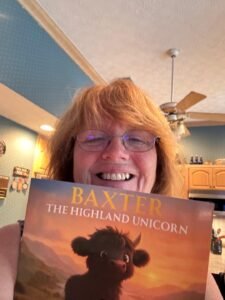 Woman holding copy of Baxter the Highland Unicorn up near her face in front of the camera