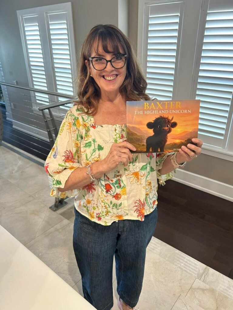 Woman standing in front of windows holding up a copy of Baxter the Highland Unicorn