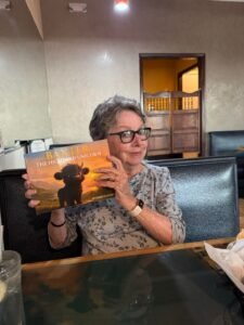 Woman sitting down holding up a copy of Baxter the Highland Unicorn